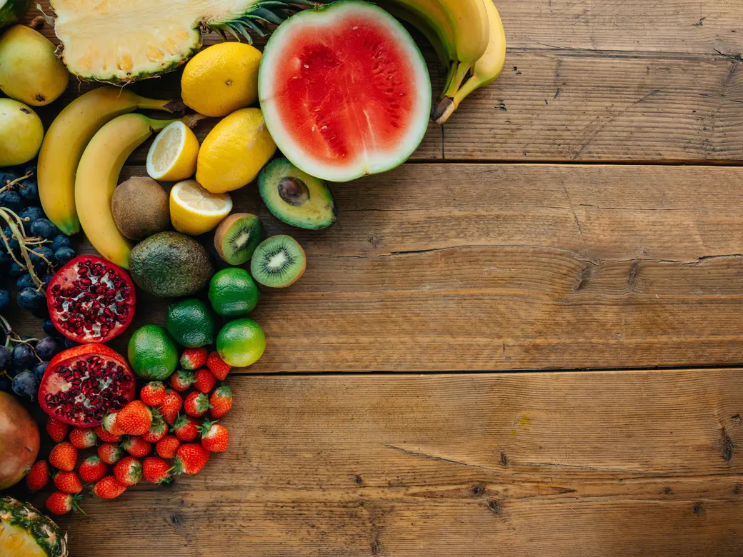 Fresh fruit — watermelon, citrus, berries, kiwi, and pomegranate — arranged across a wooden table.
