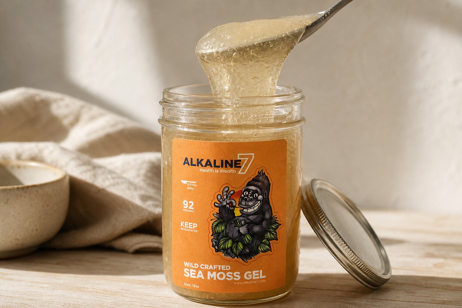 A stainless spoon lifting a thick ribbon of pale gold sea moss gel from an open Alkaline7 jar.